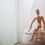 A wooden toy seated on a toilet